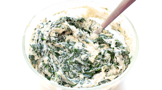 Spinach and ricotta white sauce in a mixing bowl with a spoon.