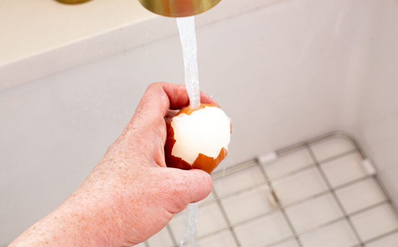 Hand peeling an egg under running water.