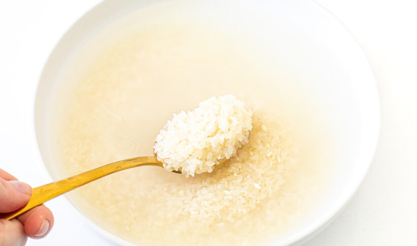 Sushi rice in a bowl of water with a spoon showing the grains of rice.