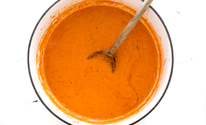 Creamy Roasted Red Pepper and Tomato Soup in a dutch oven with a wooden spoon