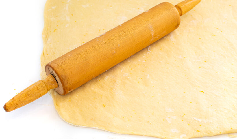 Dough being rolled into a rectangle with a rolling pin.