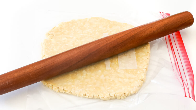 Pie dough in a zip lock bag being rolled out with a rolling pin.
