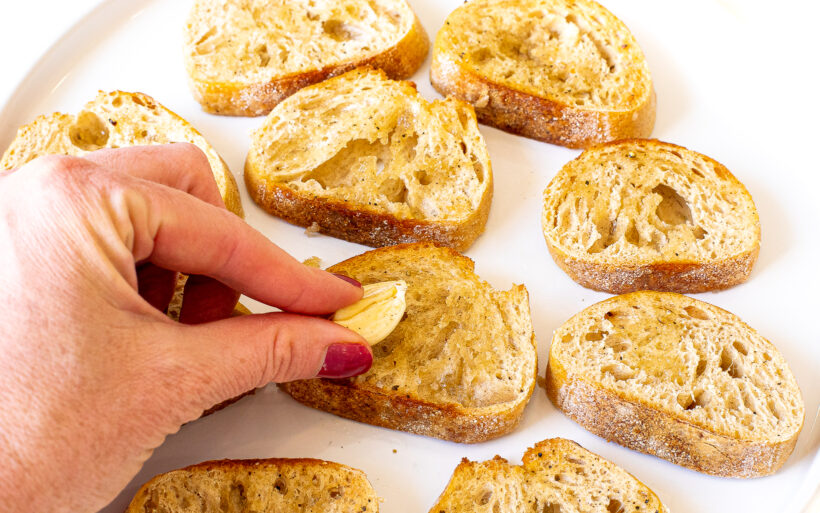 rubbing garlic clove on top of toasted baguette