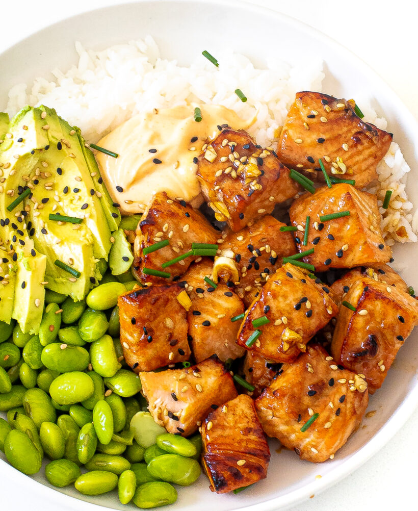 Salmon bites served in a white bowl with edamame, avocado and rice. 