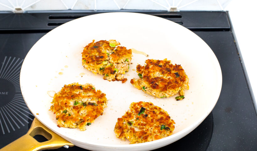 Cooked salmon cakes in a white skillet.