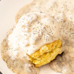 Sausage gravy poured on top of a biscuit on a white plate.