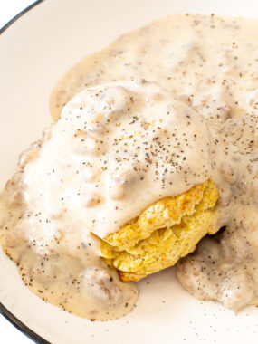 Sausage gravy poured on top of a biscuit on a white plate.