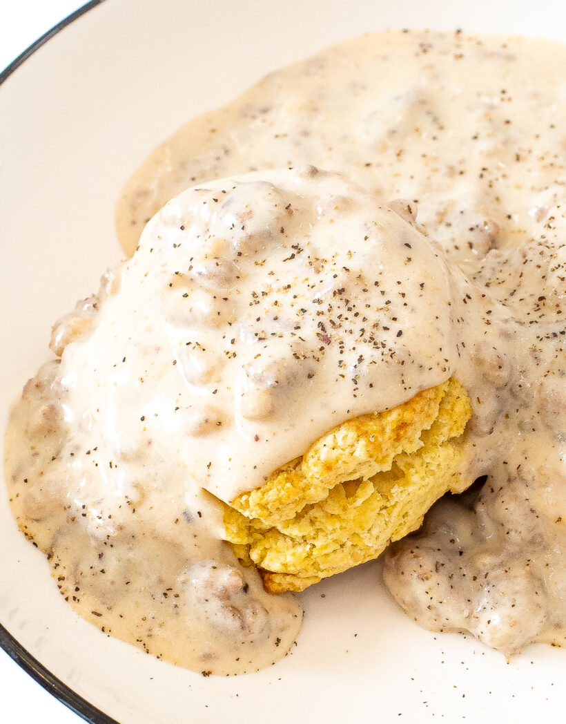 A fluffy biscuit topped with sausage gravy on a white plate.