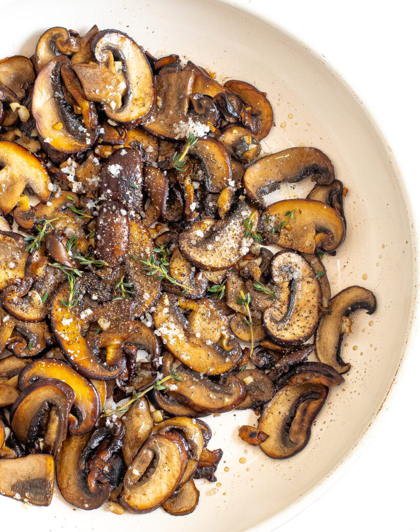 Overhead shot of sauteed mushrooms in a skillet topped with salt and thyme.