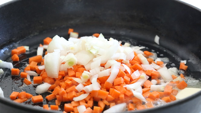 adding onions and carrots to a large cast iron skillet