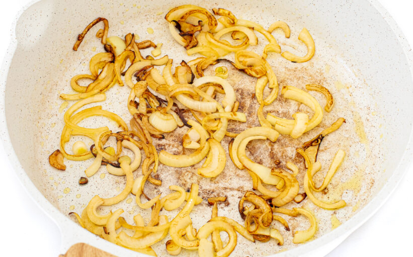 Sauteed sliced onions in a white frying pan.