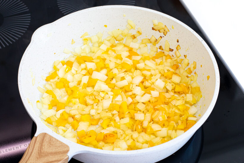 Onions and bell pepper sautéing in a skillet on the stove. 