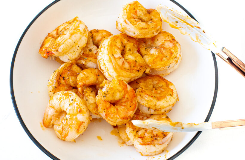 Tongs holding shrimp in a skillet.