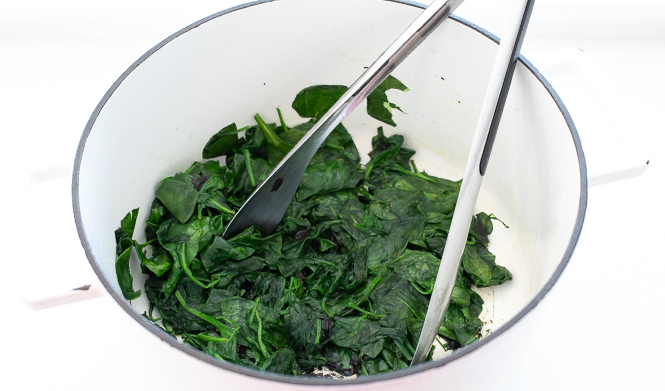 Spinach in a clear bowl with tongs.