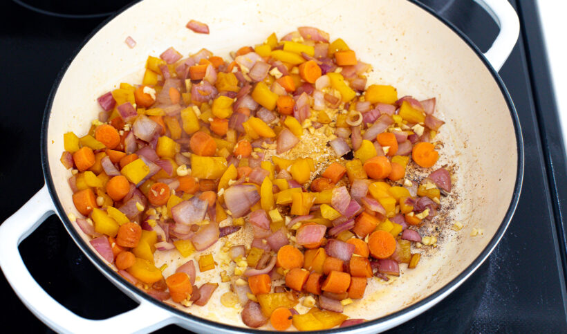 Vegetables sautéing in a white pan.