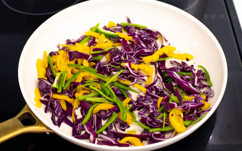 Veggies being sautéed in a white skillet on the stove. 