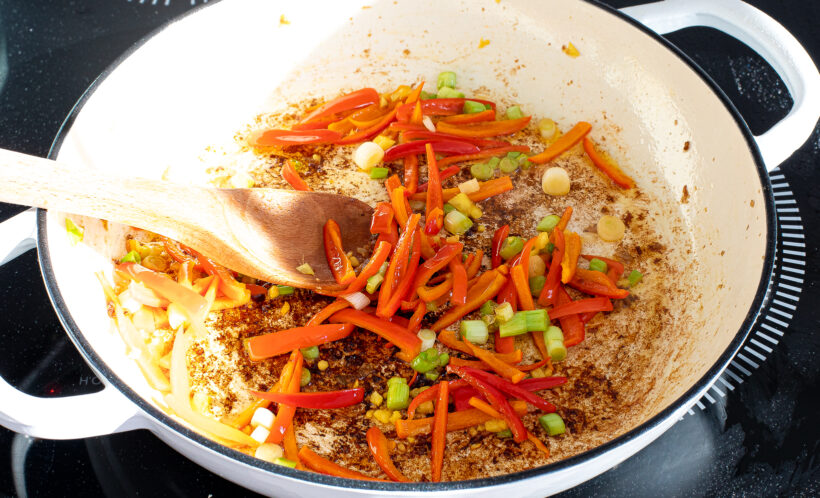 Vegetables being sautéed in a skillet on the stove. 
