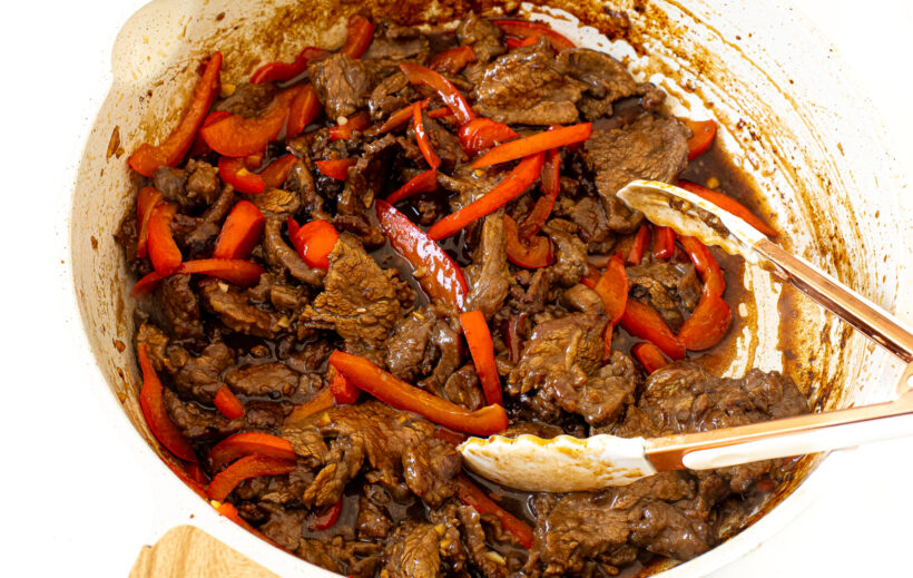 Szechuan beef in skillet with white tongs