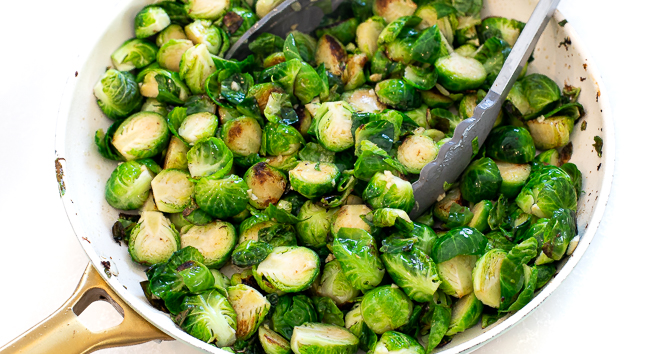 Brussels sprouts being sauteed in a white pan.