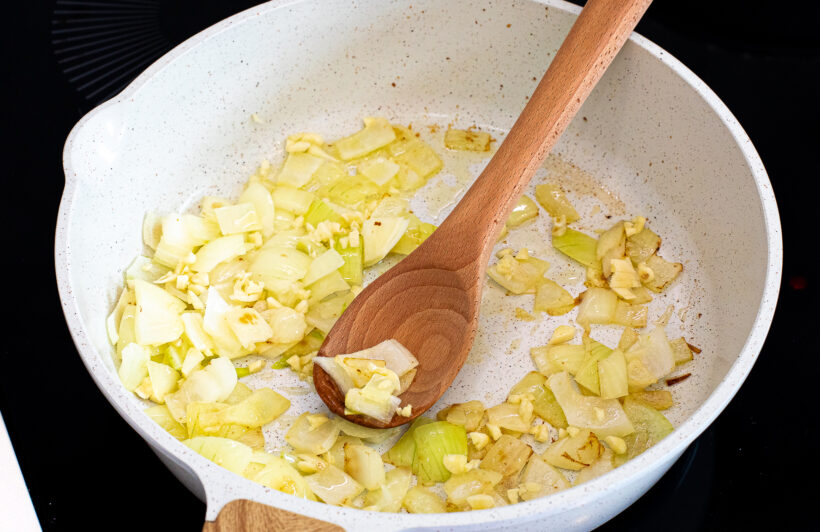 Onions and garlic cooking in a skillet on a stove. 