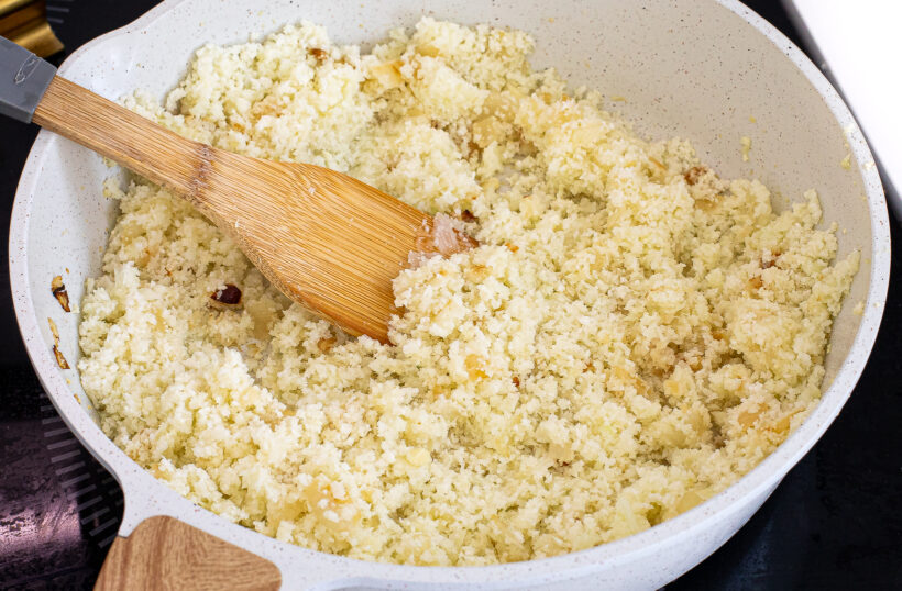 Riced cauliflower being mixed with the onion and garlic in the pan.