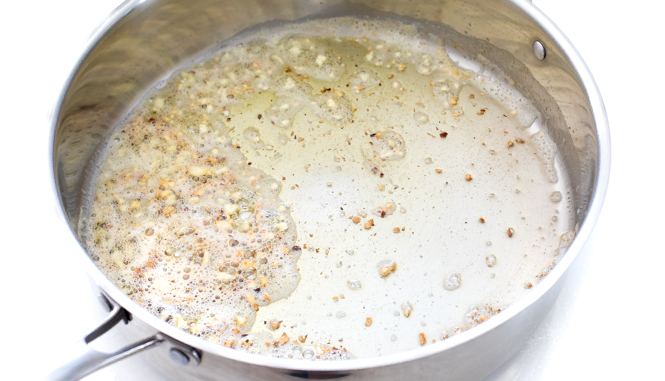 A silver frying pan with oil and garlic.