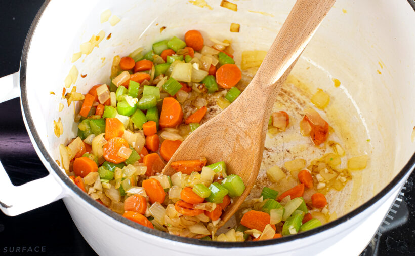 Carrots, celery and onions being sautéed in a large soup pot. 