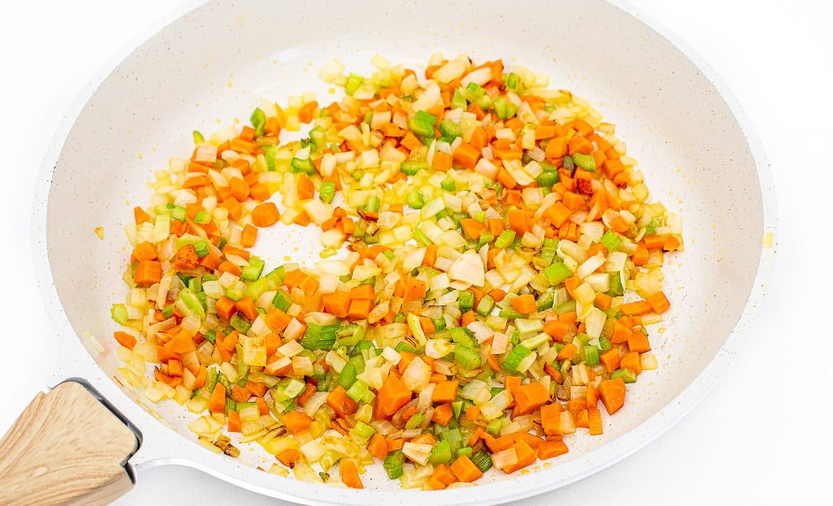 Sautéing mirepoix in a white skillet.