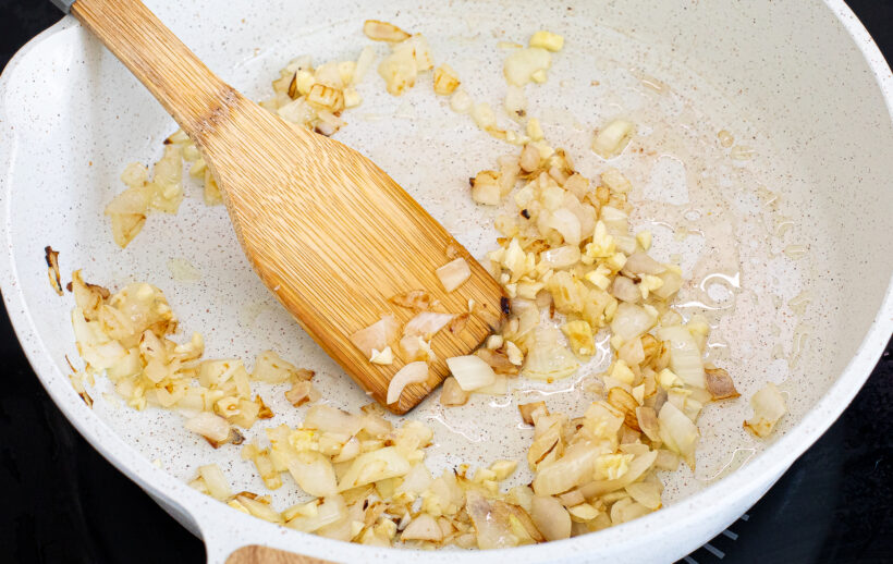 Onion and garlic sautéing in a skillet with a wooden spoon.