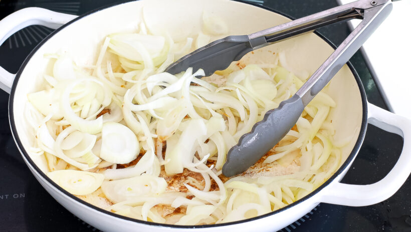 Onions cooking in a skillet with tongs.