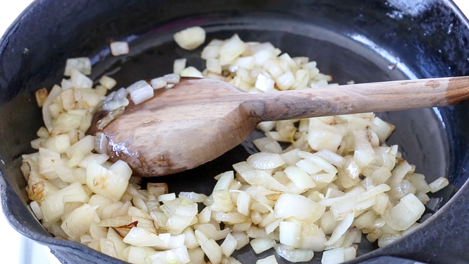 sauteed onion in cast iron skillet with wooden spoon