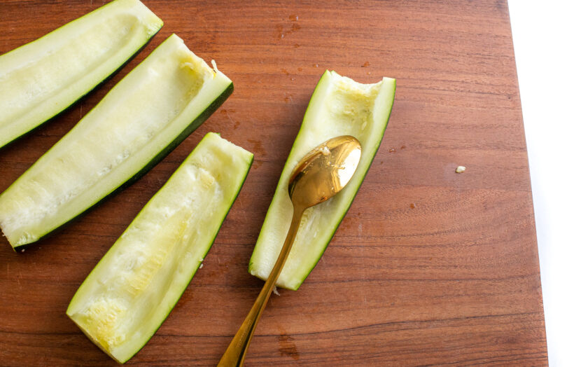 Using a spoon to scoop out the seeds of the zucchinis.