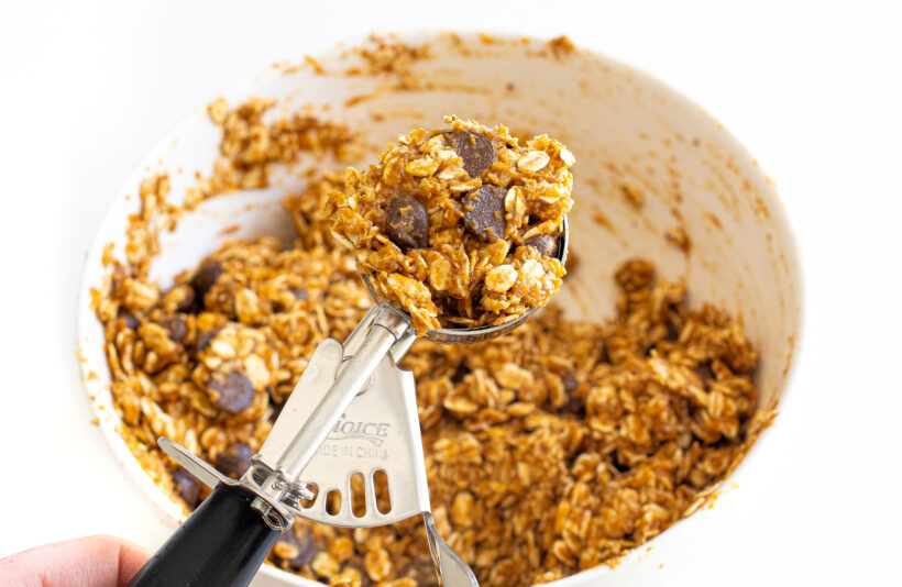 Using a cookie scoop to measure out the cookies from the mixing bowl.