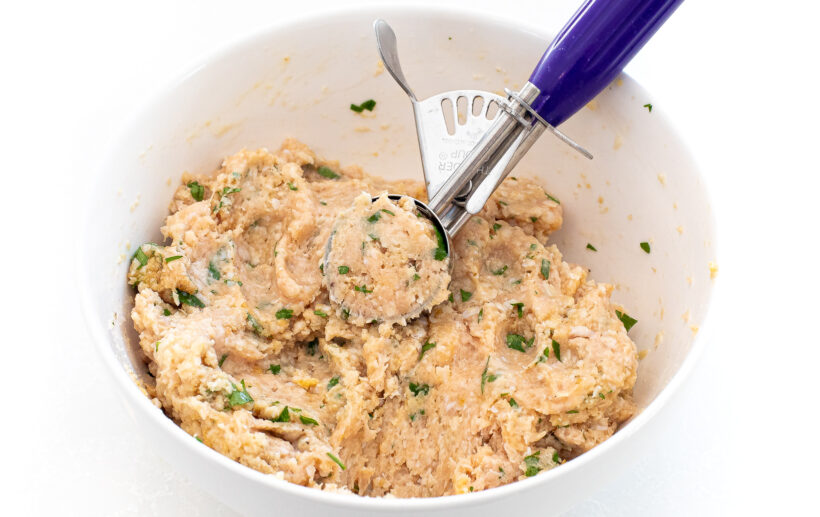 Meat mixture in a bowl with a cookie scoop to form meatballs. 