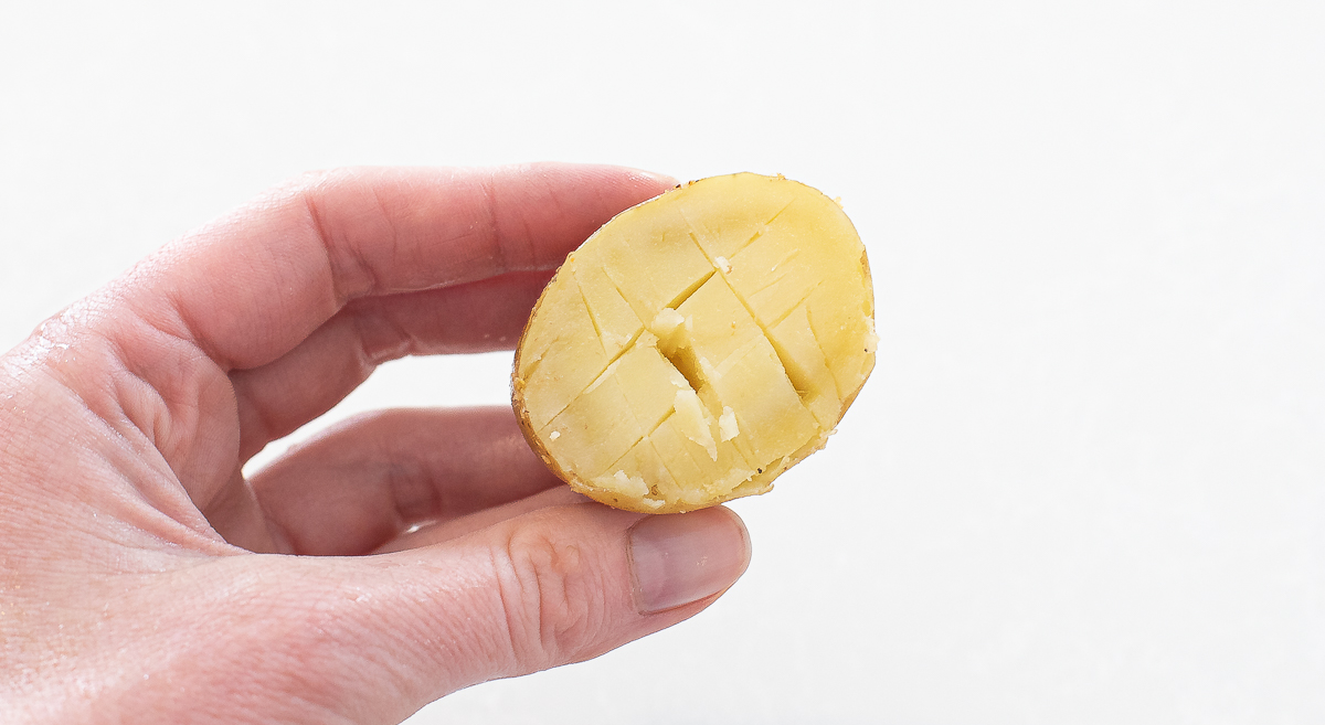 Hand holding half of potato with scored cuts into it. 