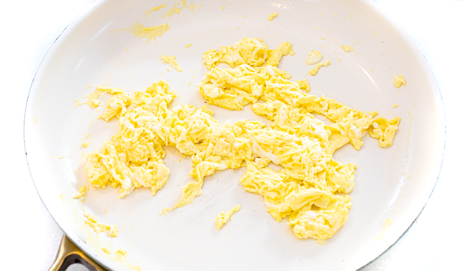 Scrambled eggs in a white skillet.