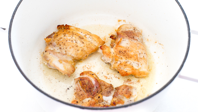 Chicken thighs searing in a white pot.