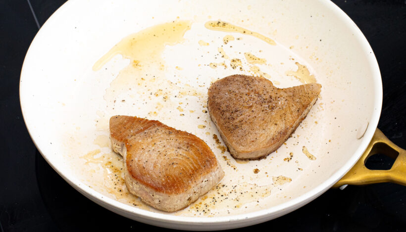 Tuna steaks being sautéed in a pan.