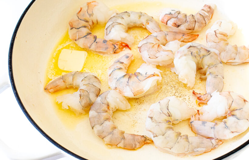 Raw shrimp cooking in a skillet with butter.