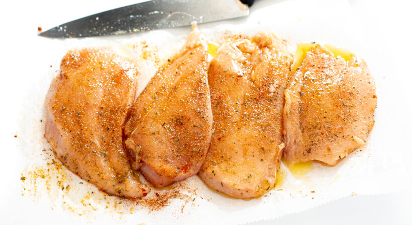 Raw chicken on a cutting board with the seasoning on it.
