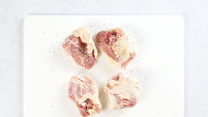 seasoning the chicken thighs on a white chopping board