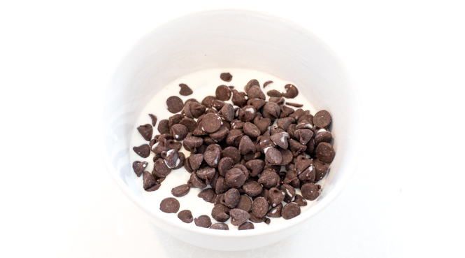 Semi sweet chocolate chips and heavy cream in a white bowl