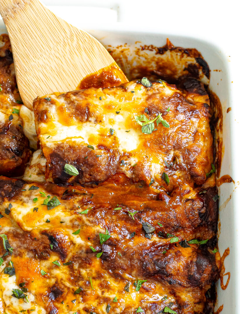 Wooden spatula scooping enchilada out of pan.