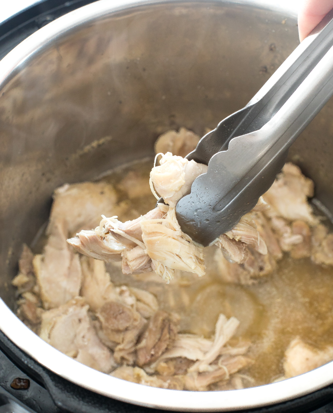 using tongs to scoop up shredded chicken thighs out of instant pot