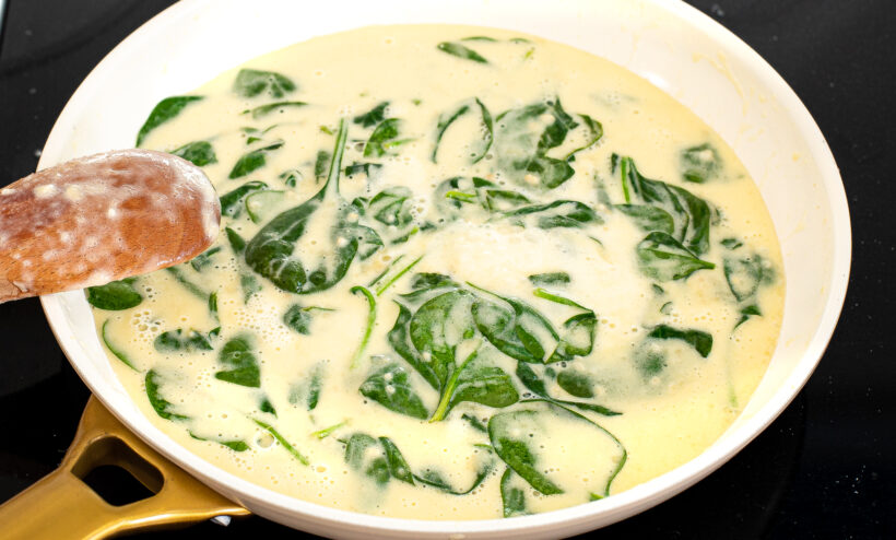 Fresh spinach added to the Alfredo sauce on the stove. 