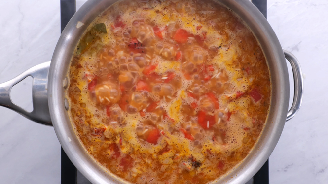 simmering rice, tomatoes and broth in silver saucepan
