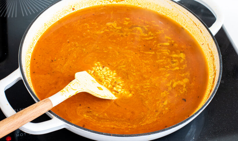 Turmeric rice with chicken broth added stirred with a spatula in a large skillet.