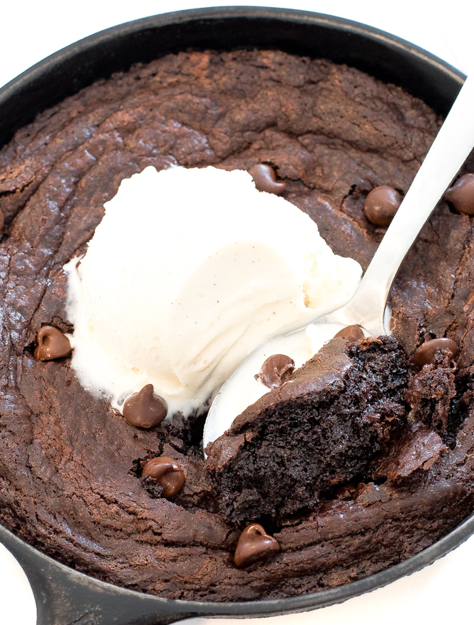 skillet brownies in cast-iron skillet with serving spoon and ice cream on top