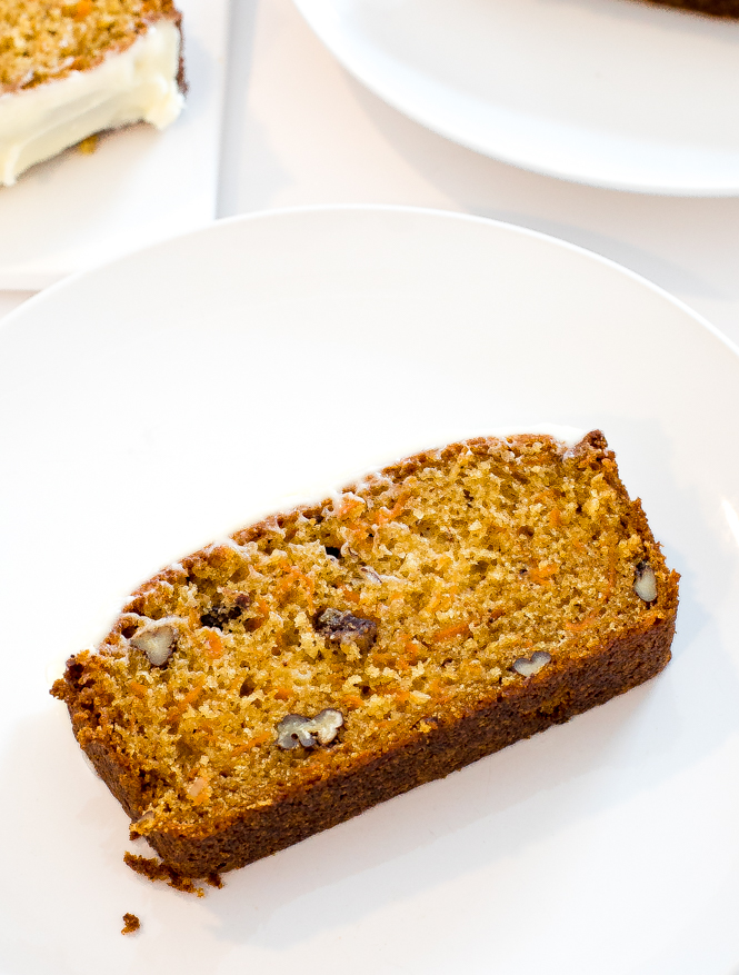 a slice of carrot loaf cake on a white plate with another slice in the background