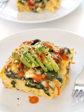 slice of breakfast casserole topped with sliced avocado on white plate